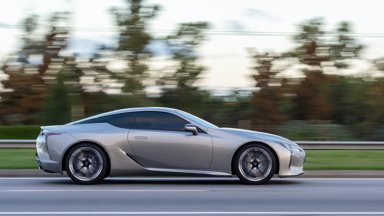 A silver sports coupe driving along a highway, photographed in motion against blurred trees
