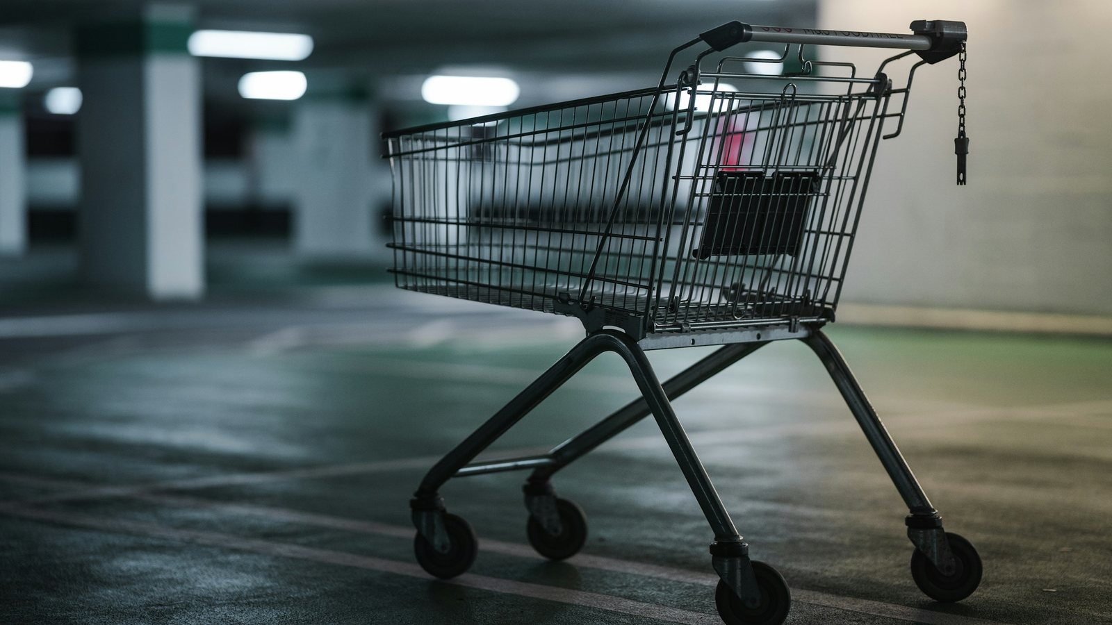 An empty supermarket trolley left alone in a dim underground car park under cold fluorescent lights
