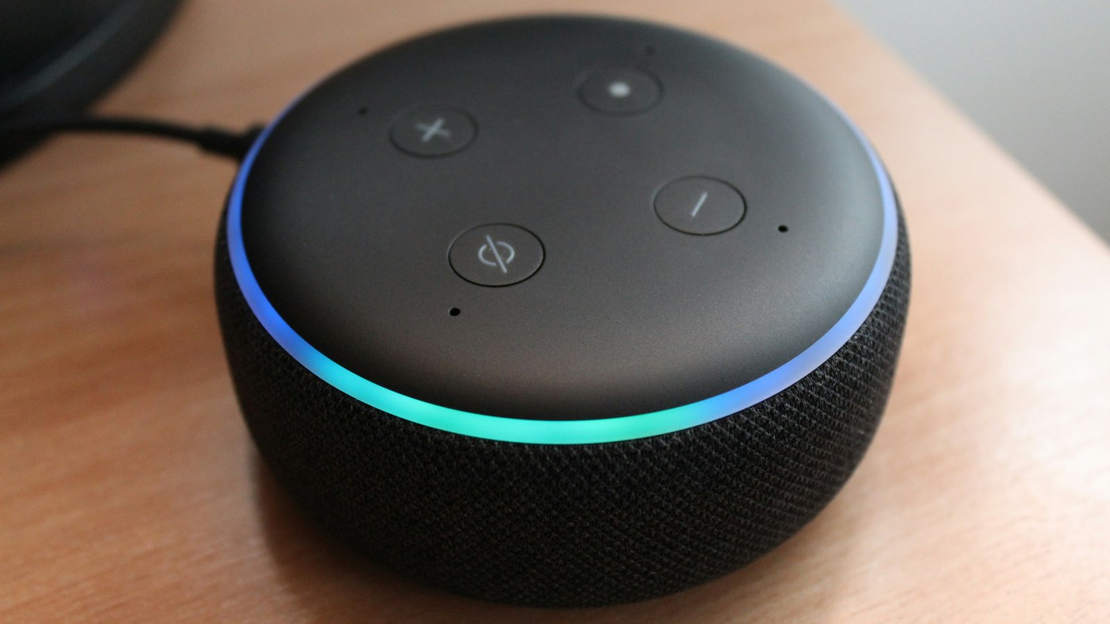 Close-up of a round smart speaker on a wooden desk, its light ring glowing blue and green
