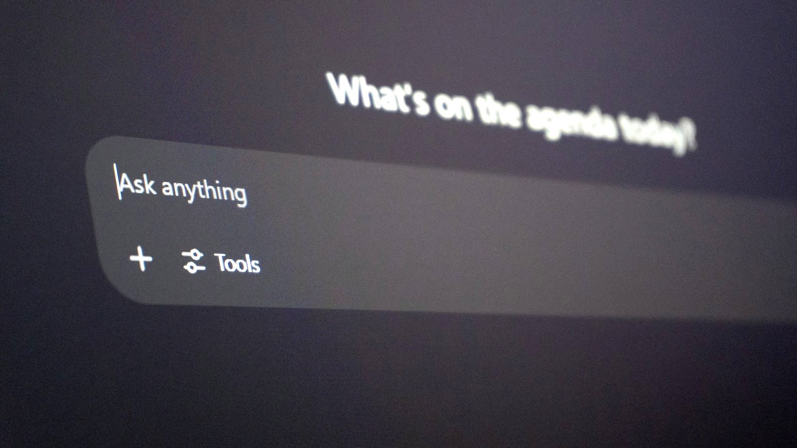 Close-up of a dark screen with an AI chat box reading 'Ask anything' and a blurred greeting above it