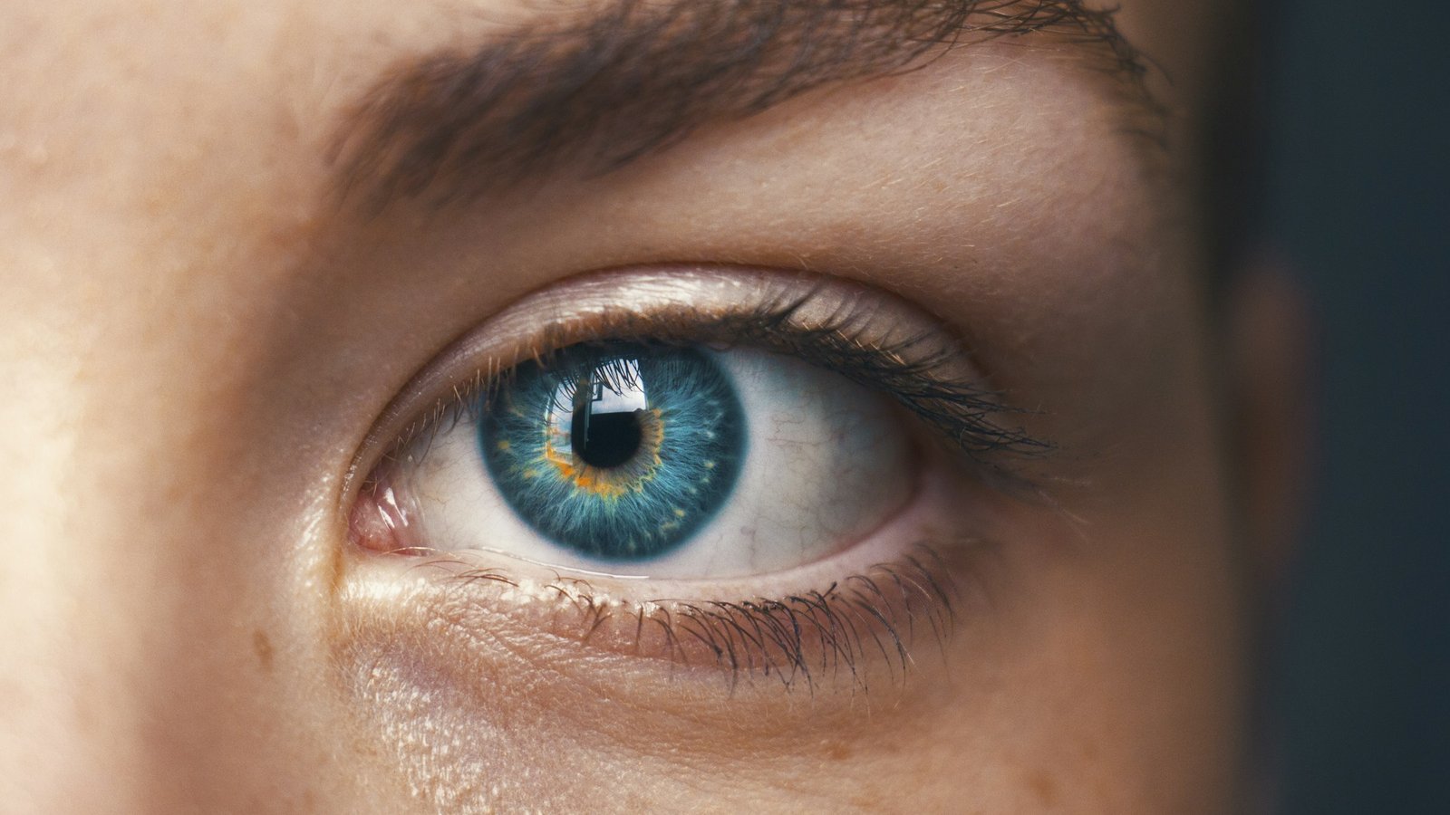 Extreme close-up of a blue-green human eye with a bright reflection in the pupil