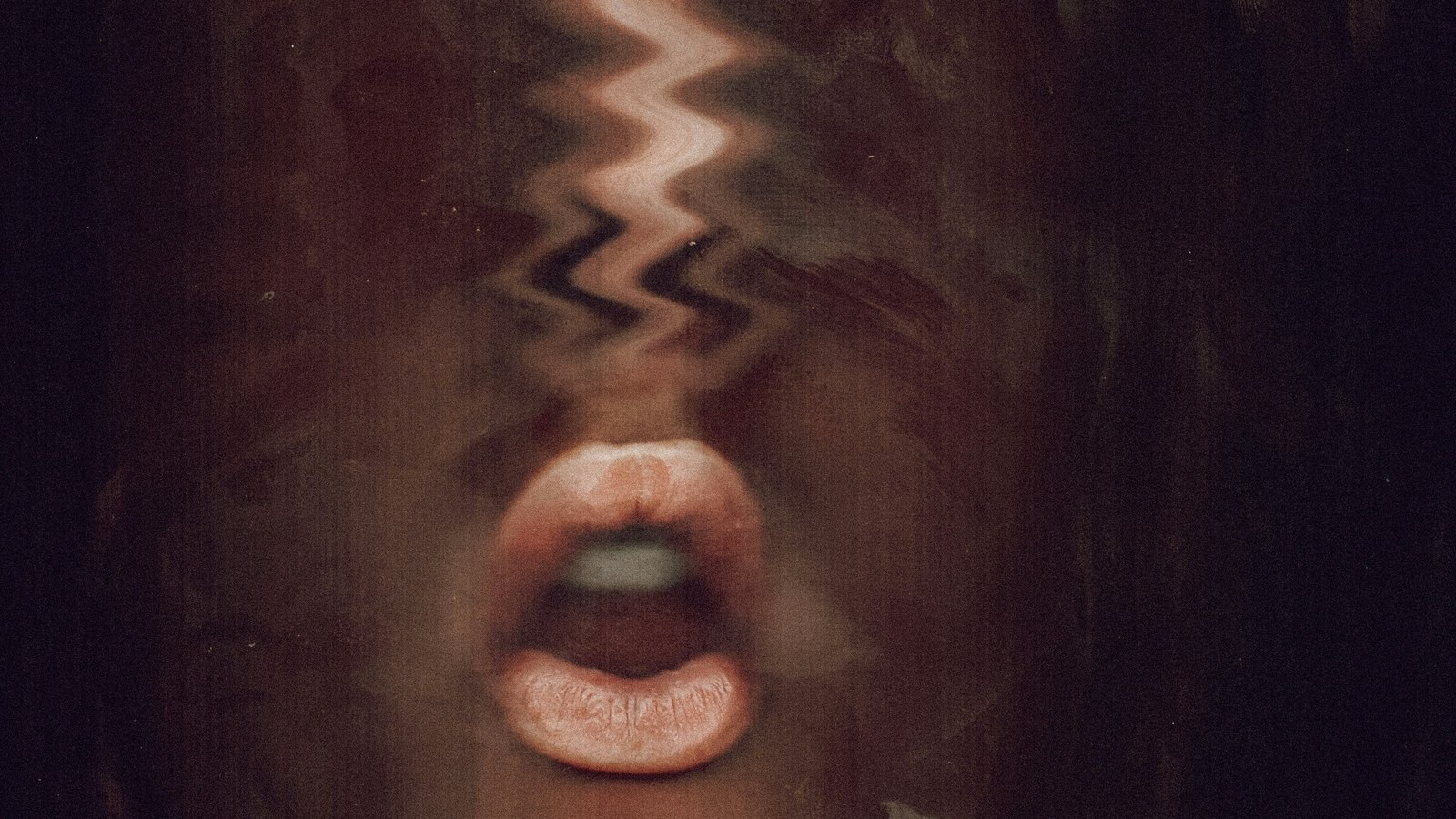 A photograph of a face seen through warped glass, the features smeared into streaks while the mouth stays sharp and open, mid-word