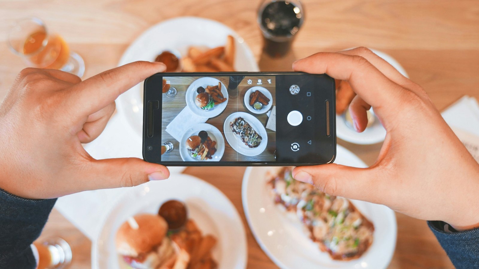 Overhead view of two hands holding a phone above a table of brunch plates, framing the food on the screen
