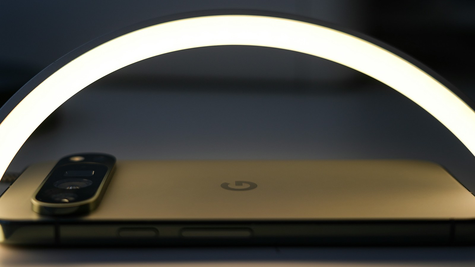A curved ring light glowing warm over a smartphone lying face down on a table in a darkened room