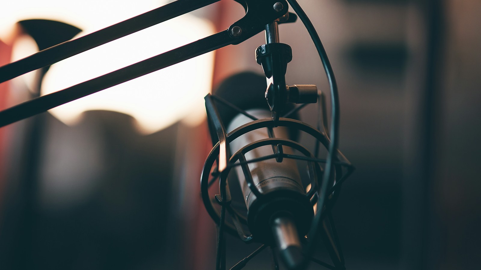 A studio microphone on a boom arm, lit from behind in warm orange, with the room behind it out of focus