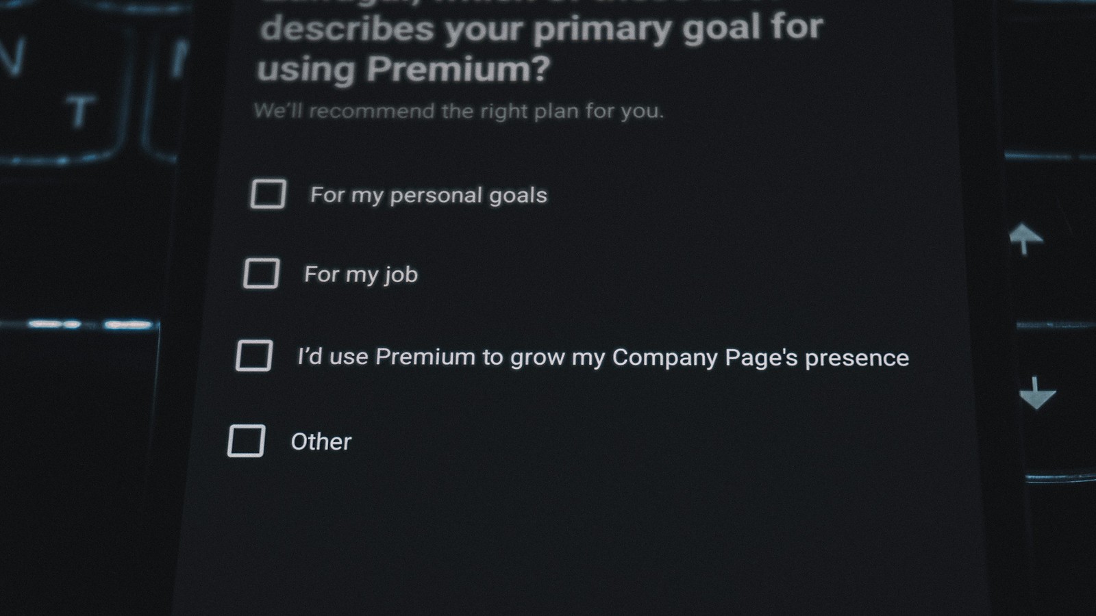 A close-up of a phone screen showing a survey question with four empty checkboxes, in front of a backlit keyboard in the dark
